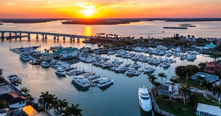 Boats in a marina at sunset with a long bridge across the water in the distance